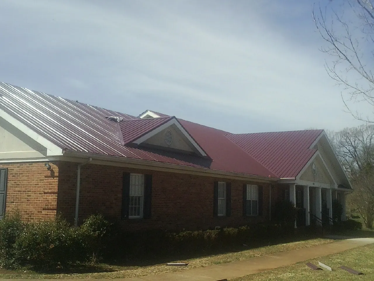 Red metal roof with gabled entries on a long brick building, from a Hail Damage Roof Repair job in Elkhart