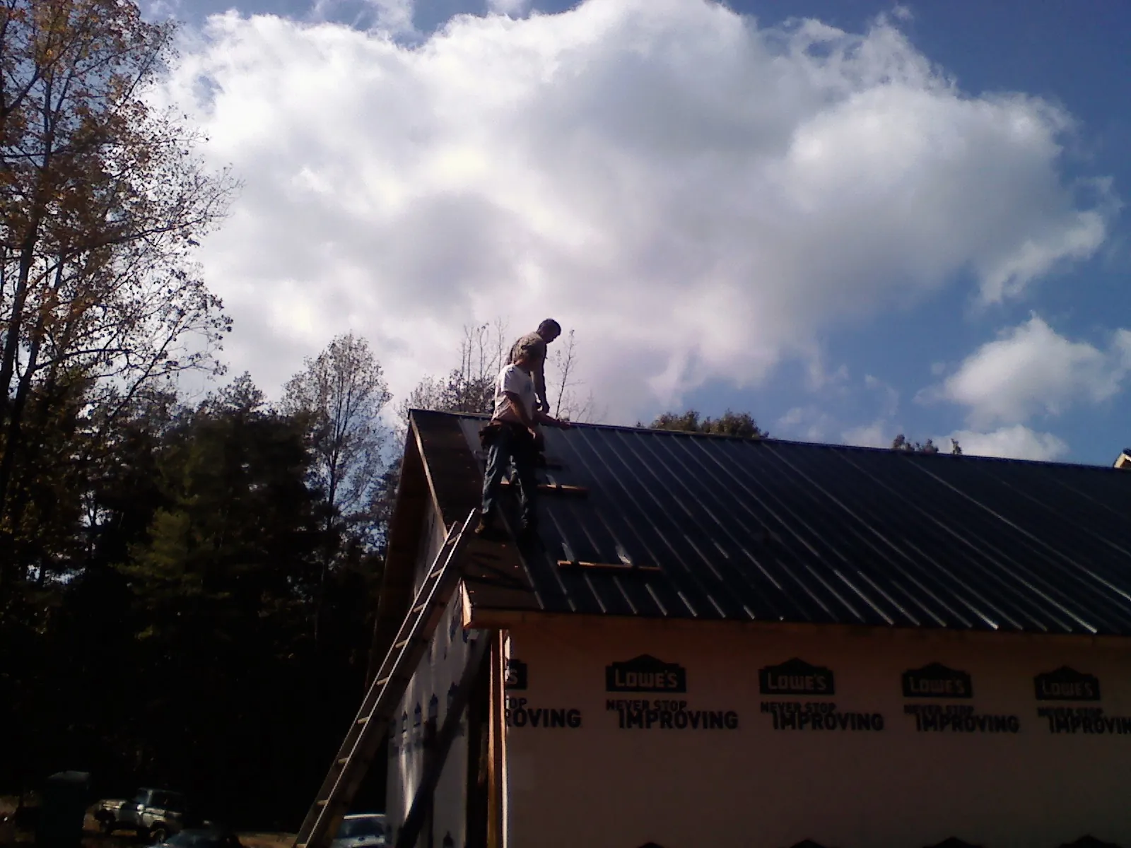 Roofer fastening dark metal panels high against a cloudy sky, from a Roof Inspection job in Elkhart