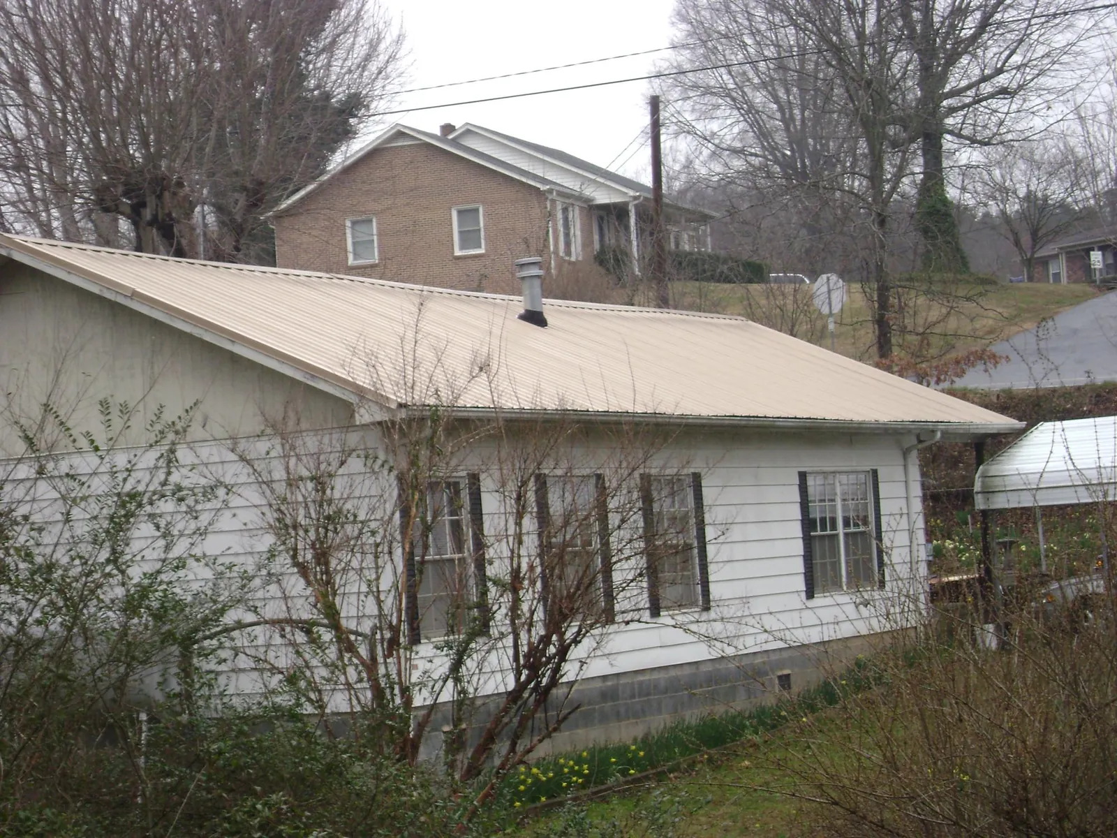 Tan metal roof on a white sided house set into a hillside — Commercial Roofing by Roofing Brothers in Elkhart
